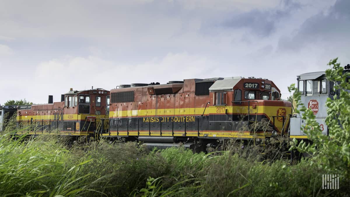 A photograph of Kansas City Southern train traveling through a grassy field.