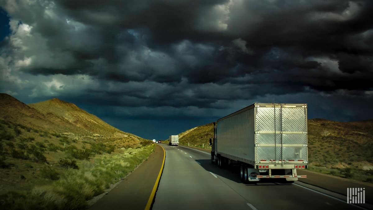 Tractor-trailers heading down a highway with dark storm cloud across the sky.