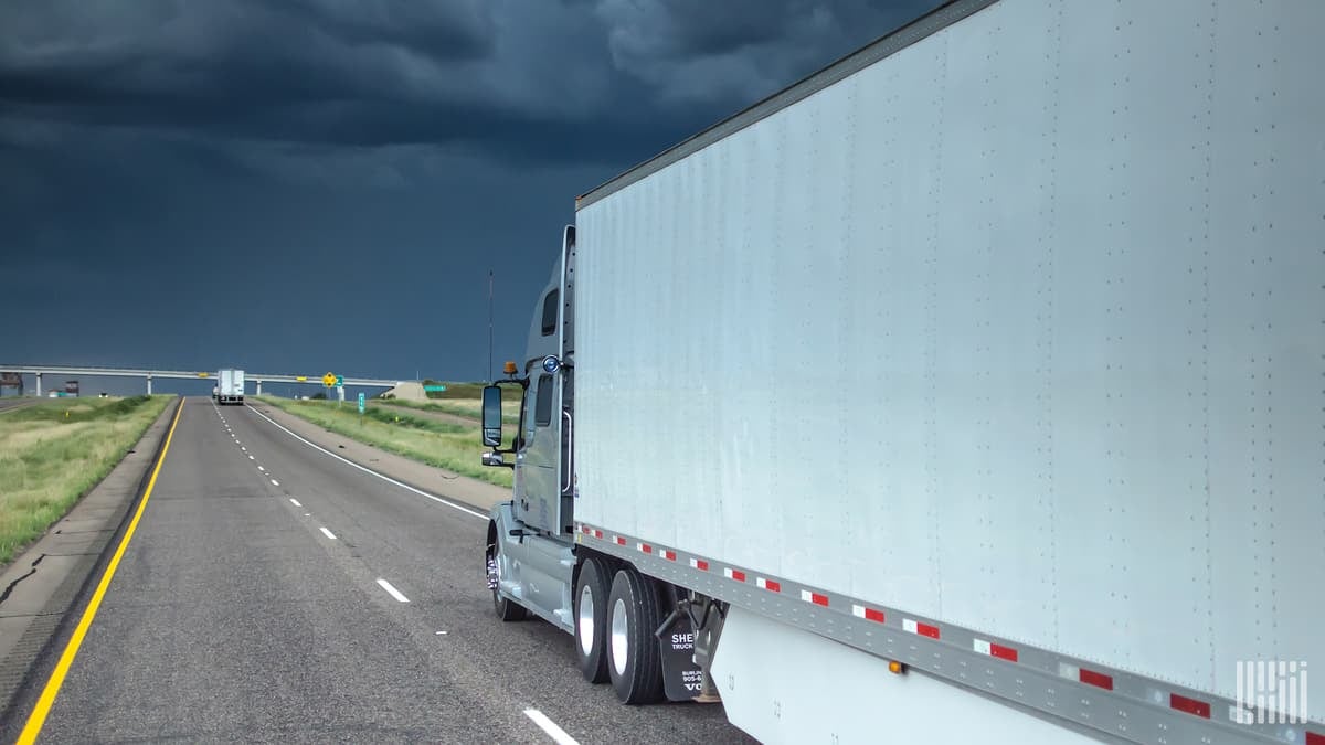 Tractor-trailer heading down a highway with storm thunderstorm cloud across the sky.