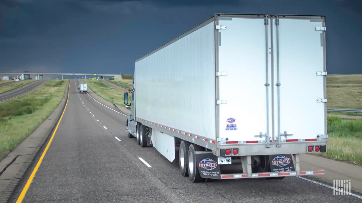 Tractor-trailers heading down a highway with storm cloud across the sky.