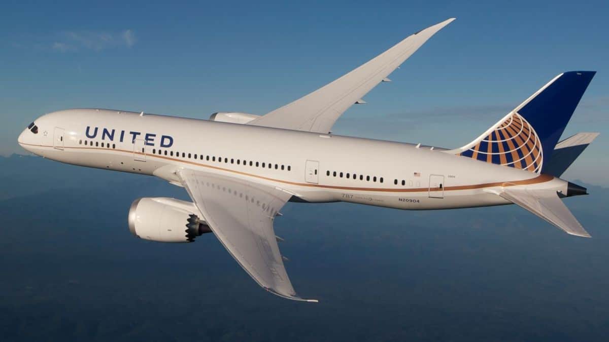 A large United Airlines jet, white with blue tail, flies high in the sky.