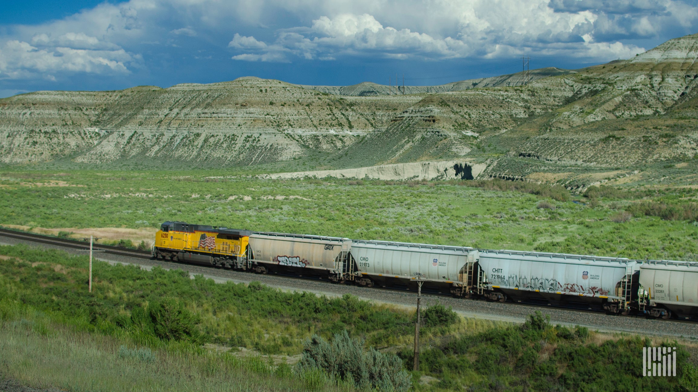 A photograph of a train hauling hopper cars across a valley.