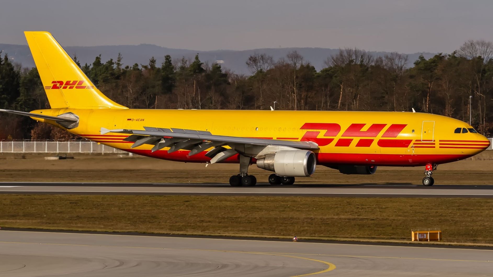 A mustard-colored DHL cargo jet on airport taxiway.