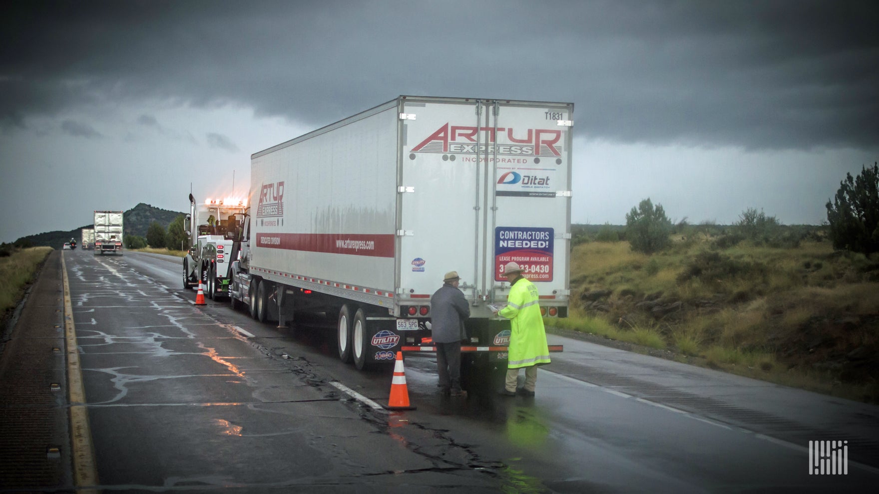 Tractor-trailer pulled over in the rain on the side of a highway.