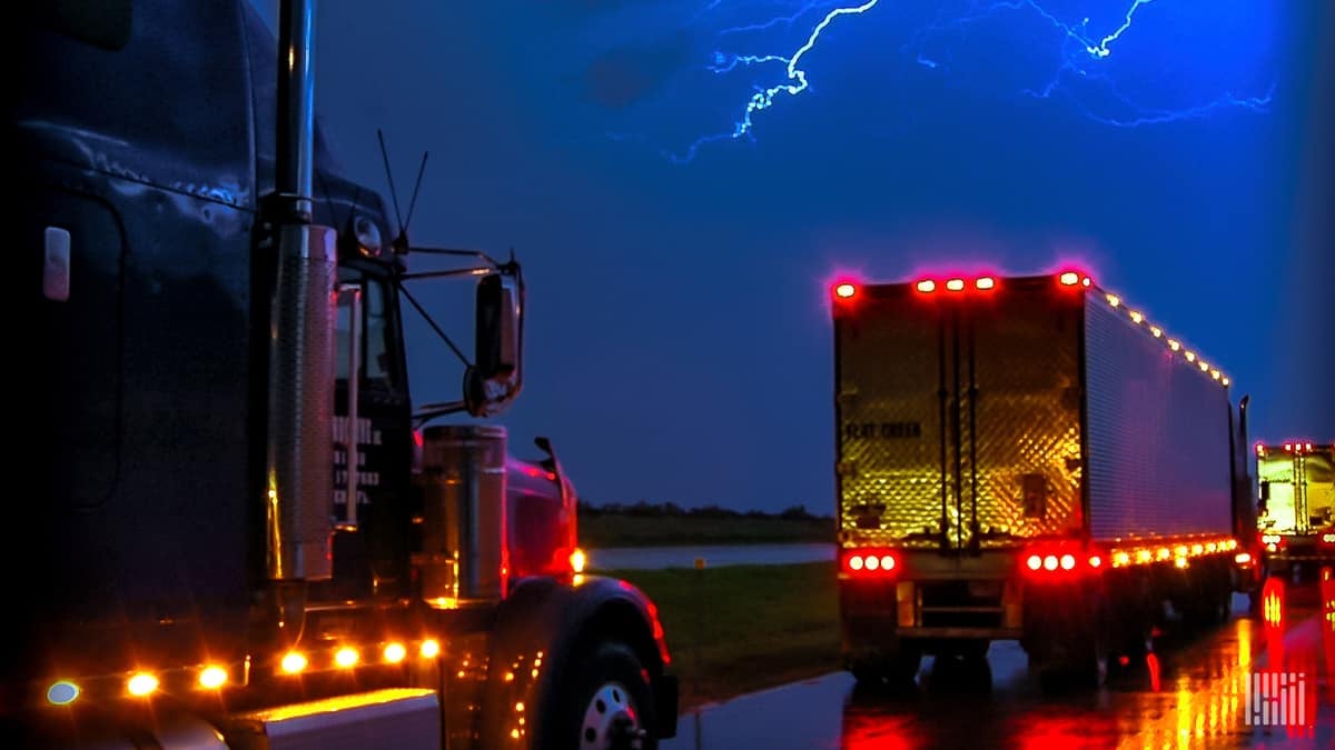 Tractor-trailers on a highway with lightning across the sky.