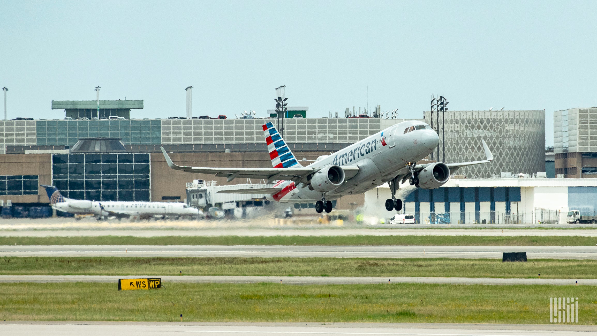 An American Airlines plane takes off with wheels just off the ground.