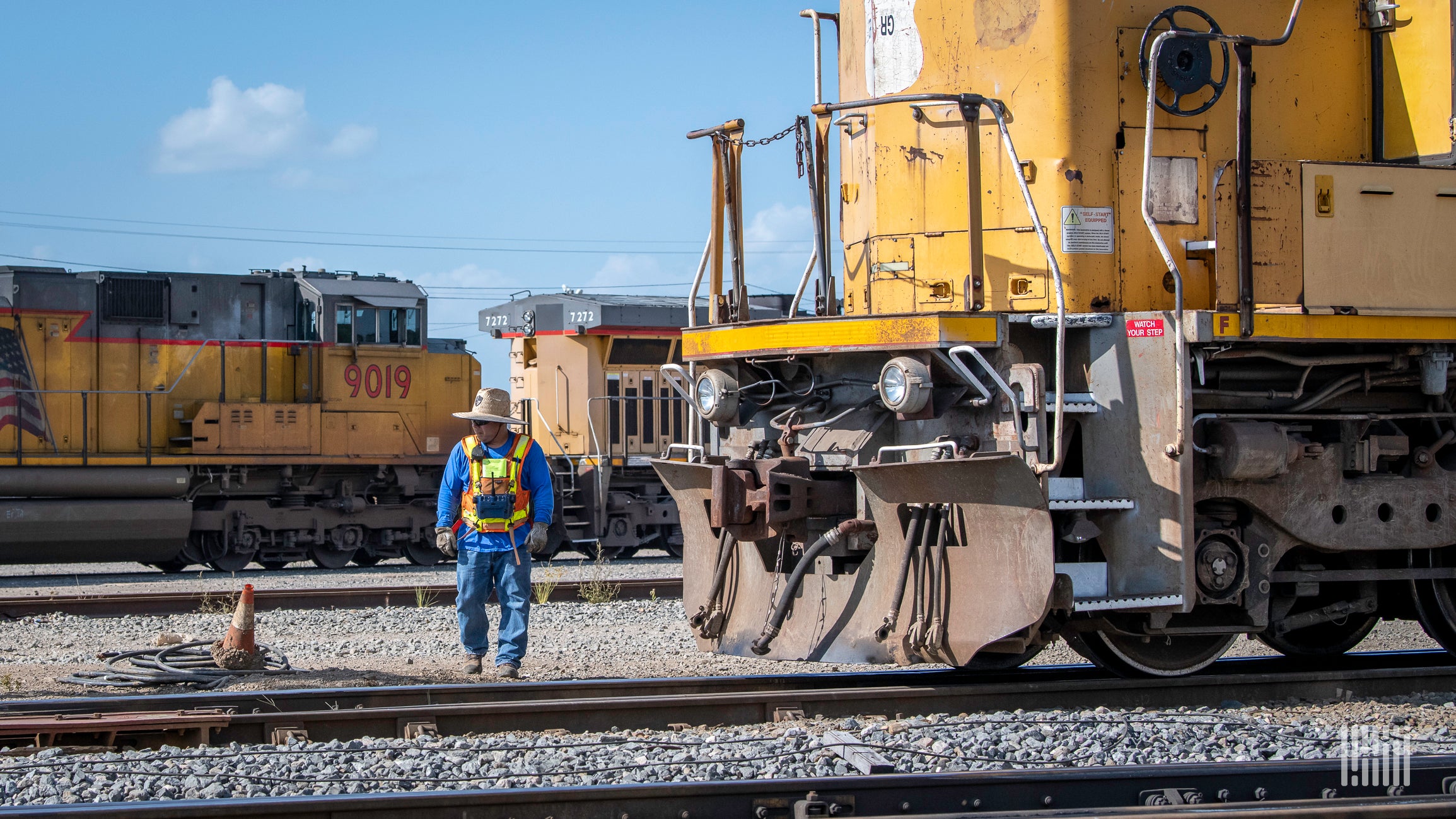 A photograph of a man walking by a locomotive in a rail yard.