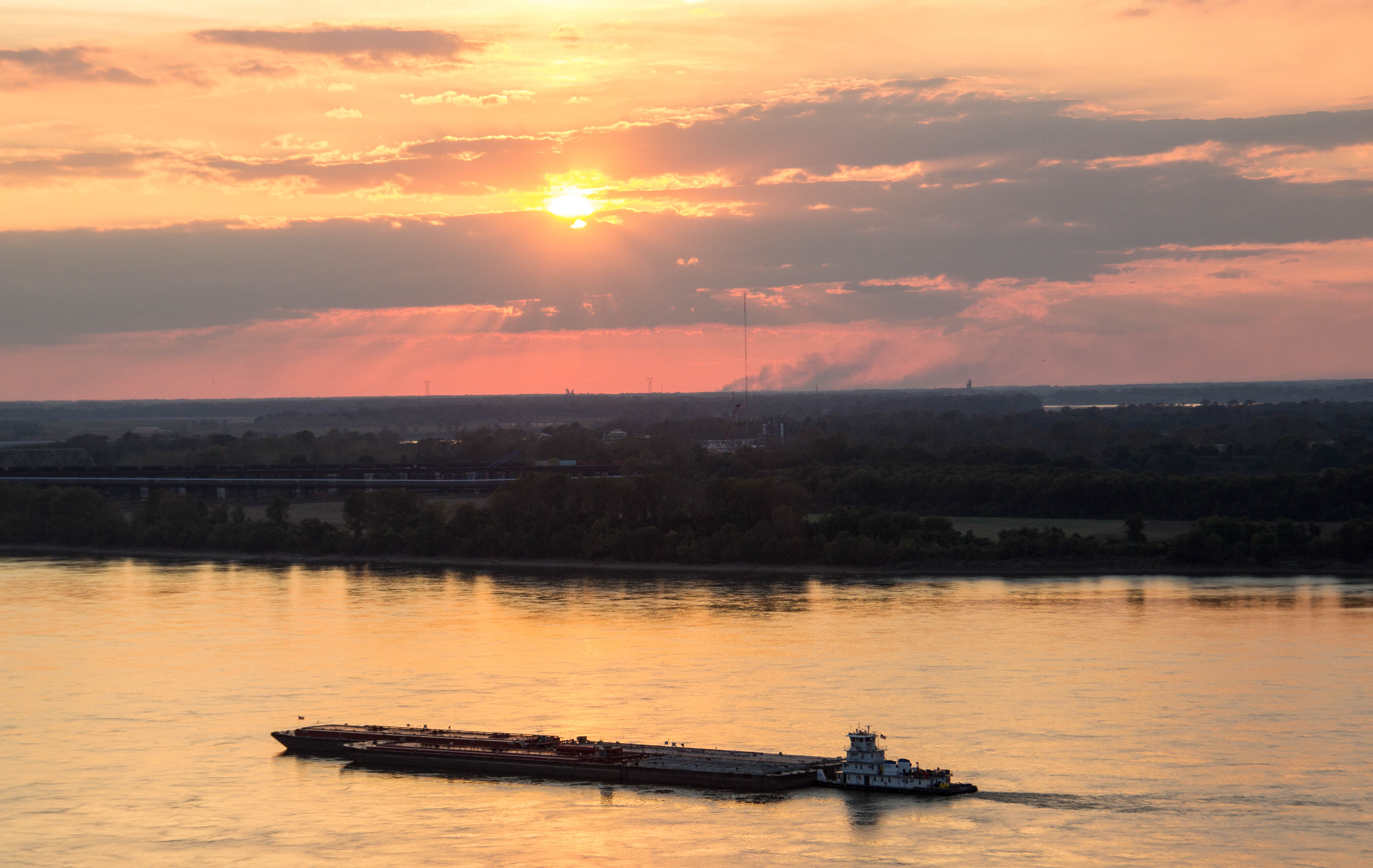 A photograph taken at sunset of a barge sailing down a river.