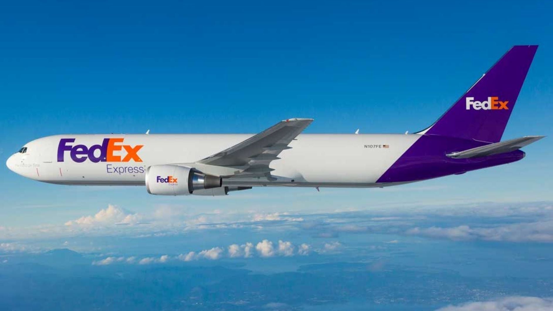 A white FedEx plane with blue tail flying above the clouds.