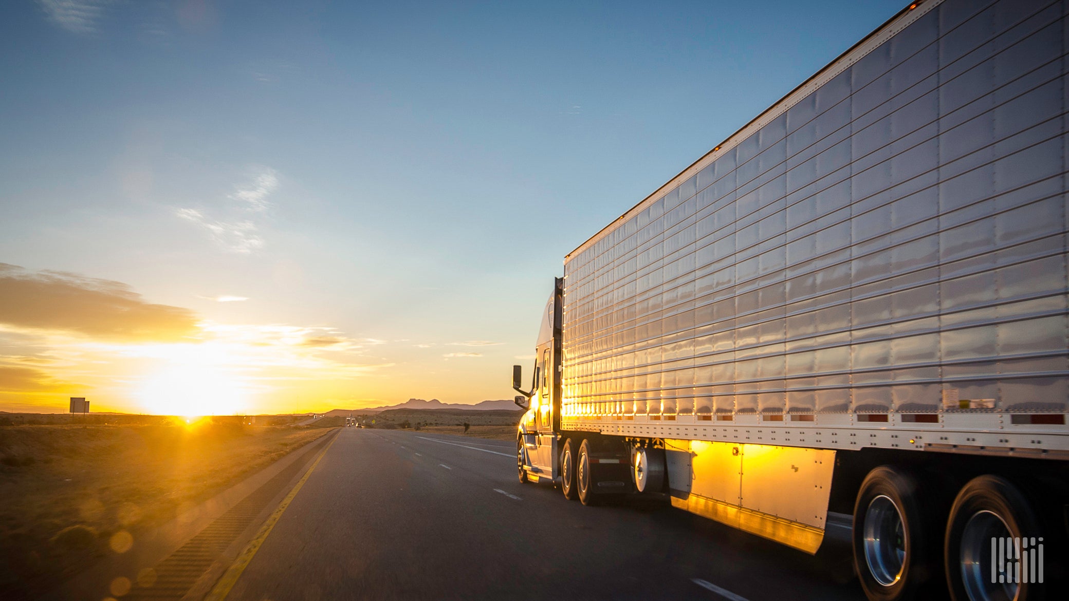 Tractor-trailer on a highway with bright su on the horizon.