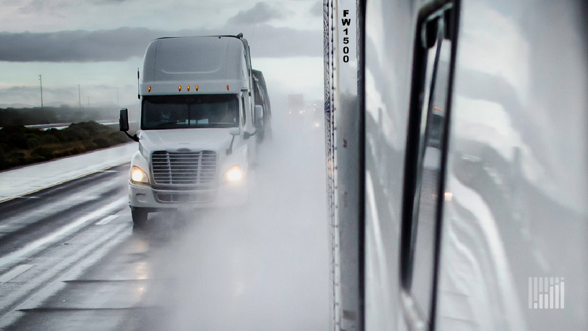 Tractor-trailers heading down a highway in the rain.