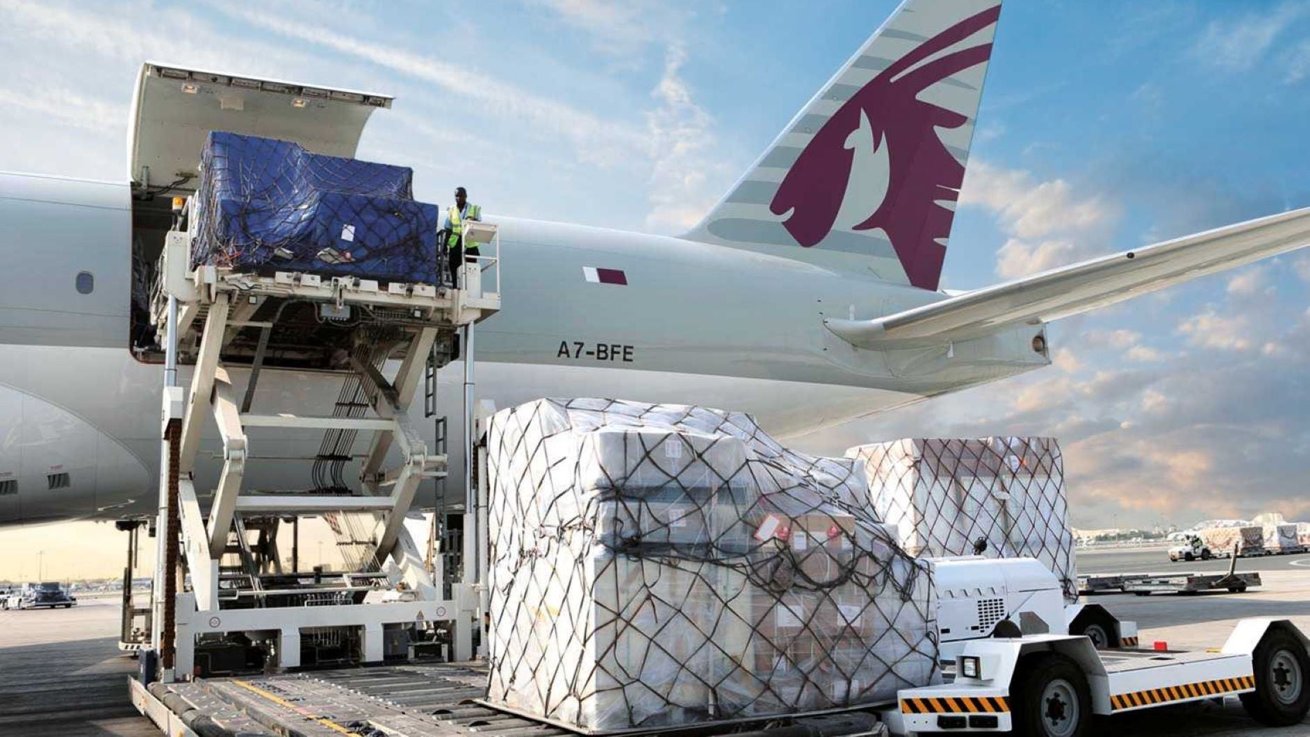 A light gray plane is loaded with cargo from the rear door using a hydraulic lift.