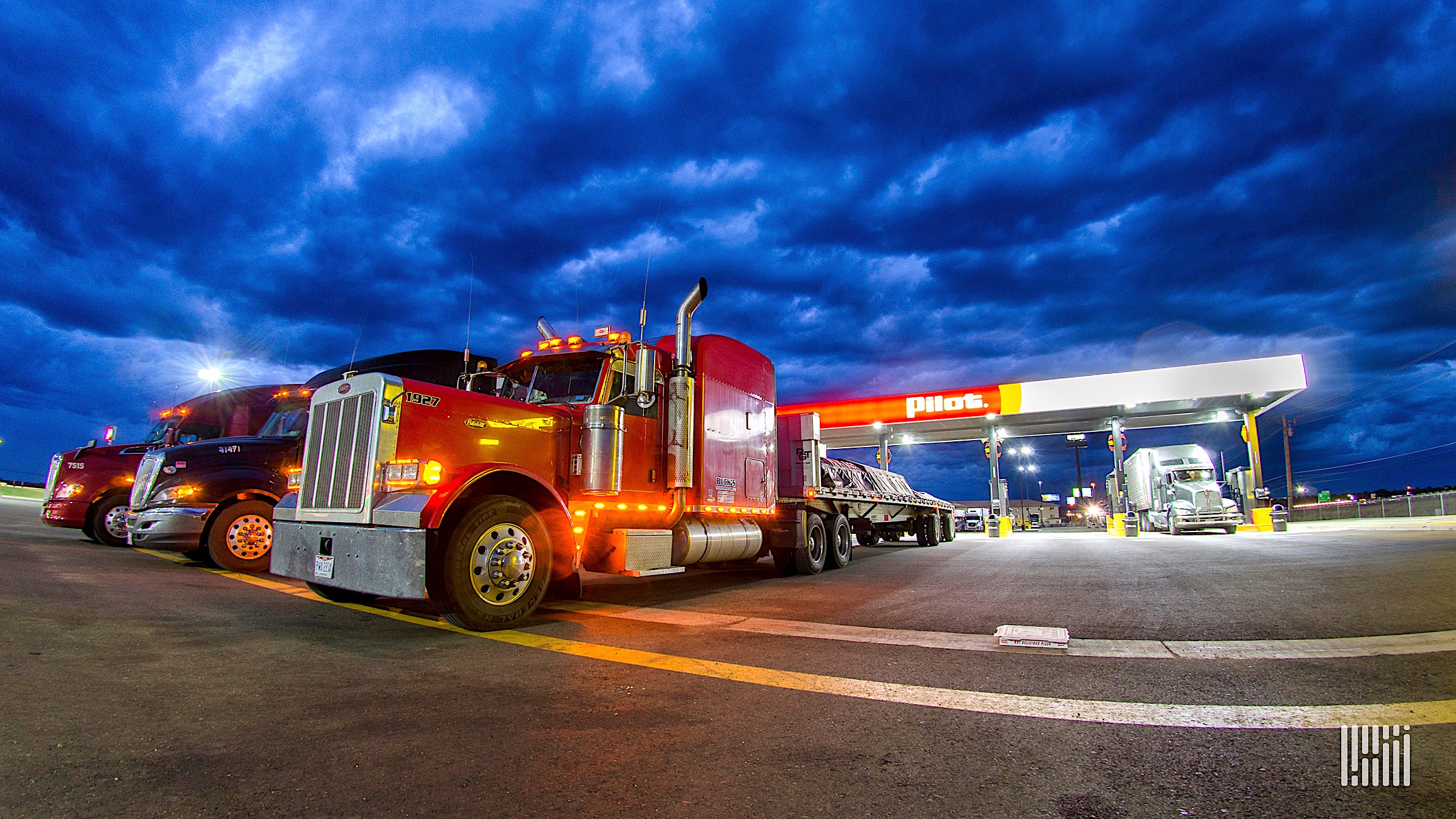 Trucks parked at a Pilot truck stock at night-time.