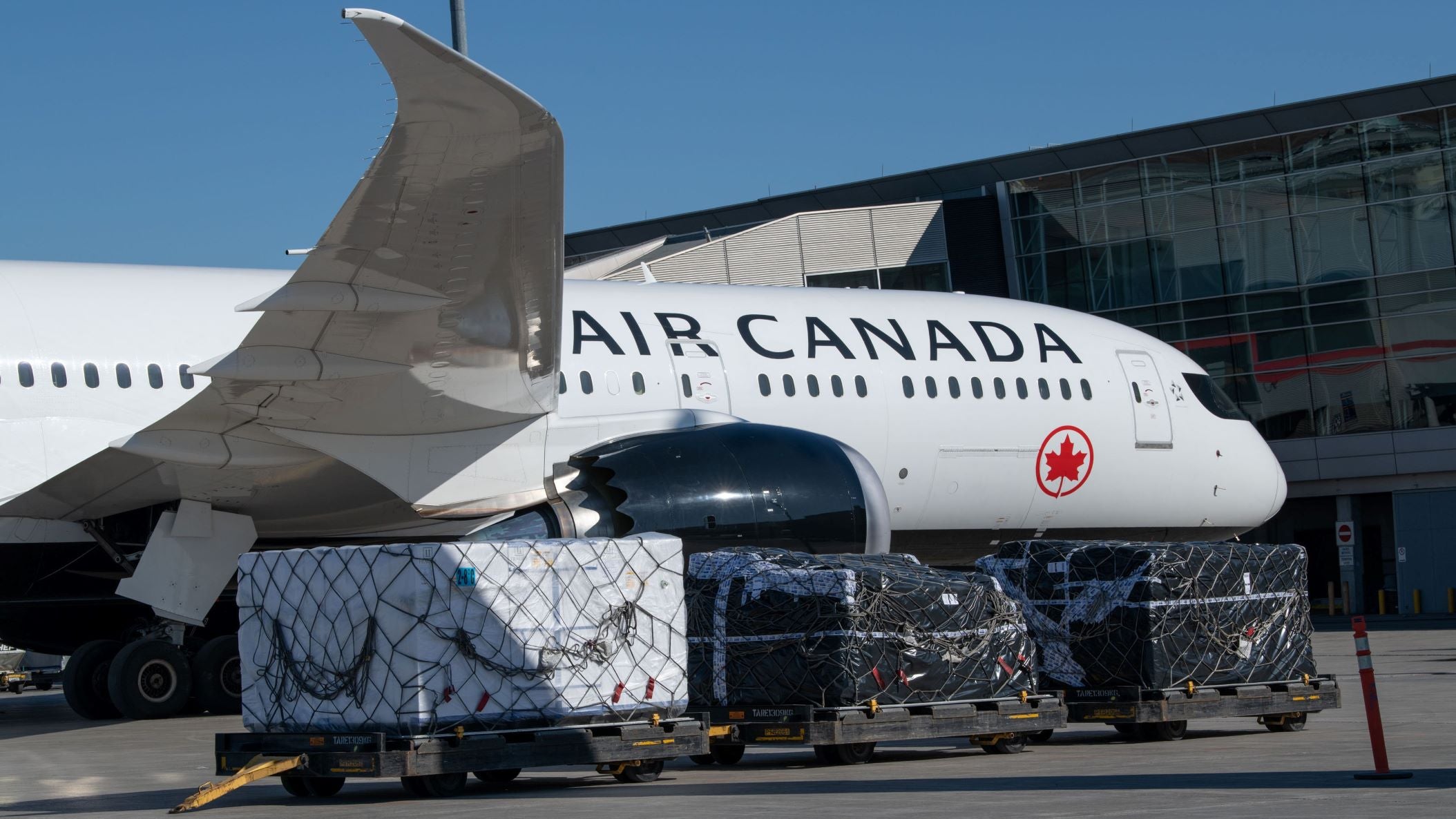 Front half of a white Air Canada jet, view from the side, with a cargo pallet in the foreground.