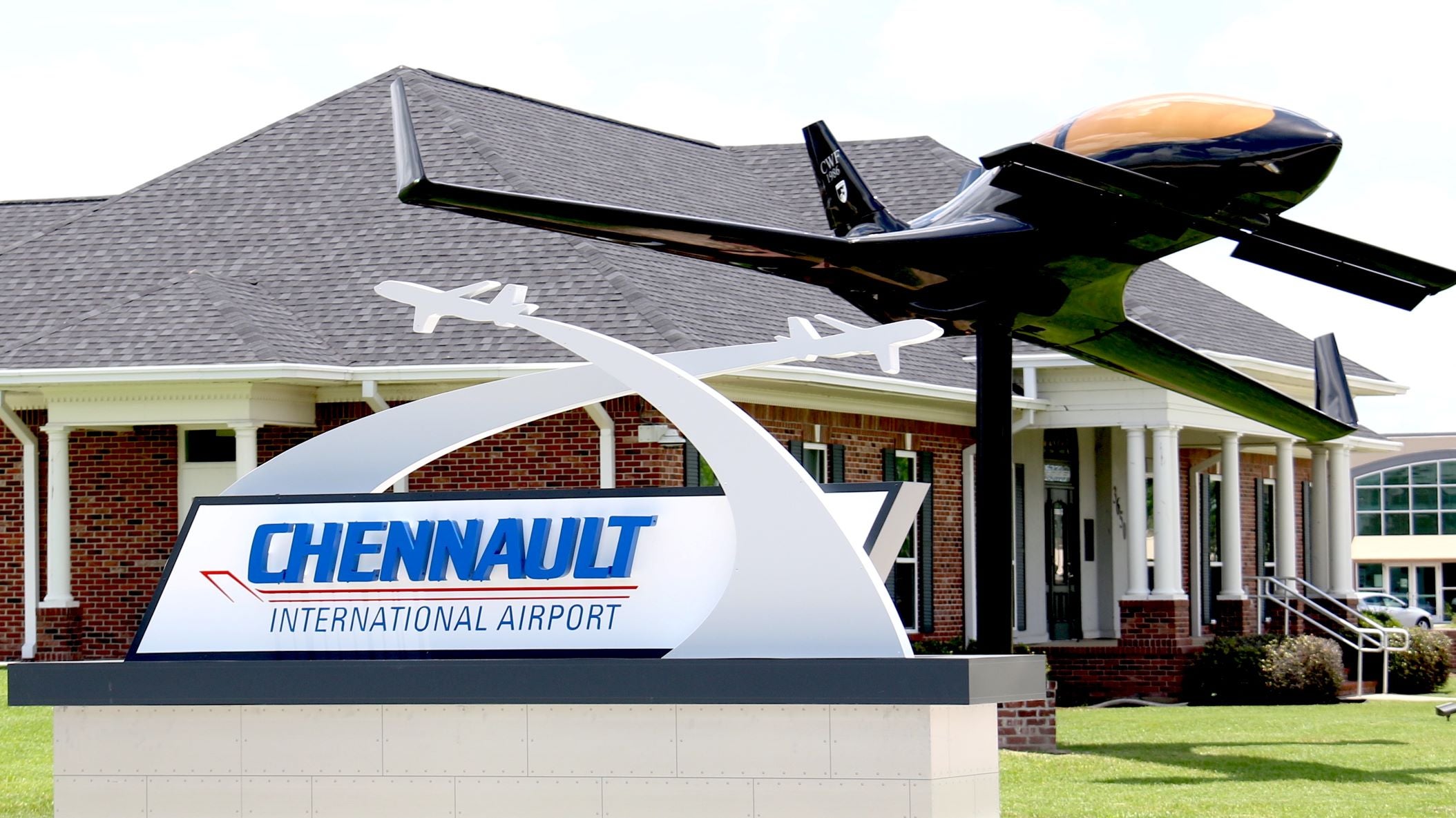 Entrance to Chennault International Airport, with sign and statue of a plane in front of small brick building.