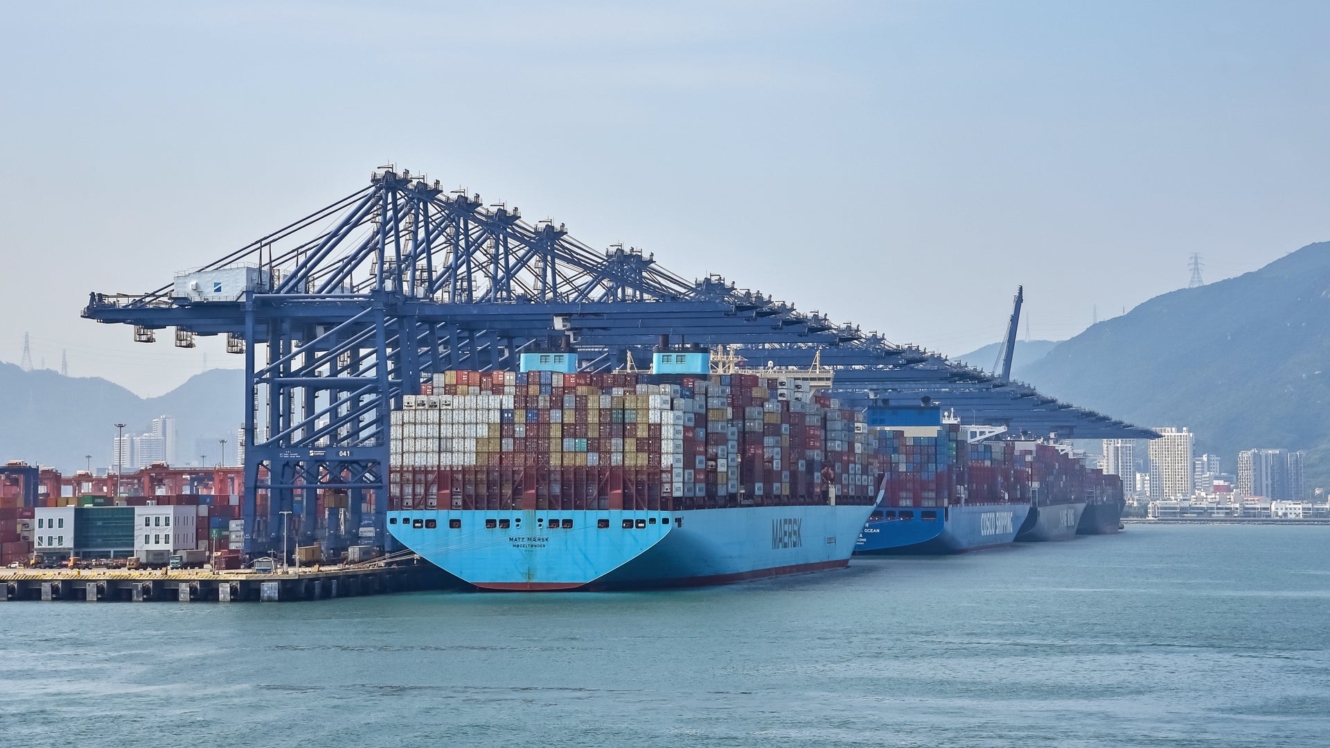 Three big container vessels in a row at a port terminal, with cranes overhead.