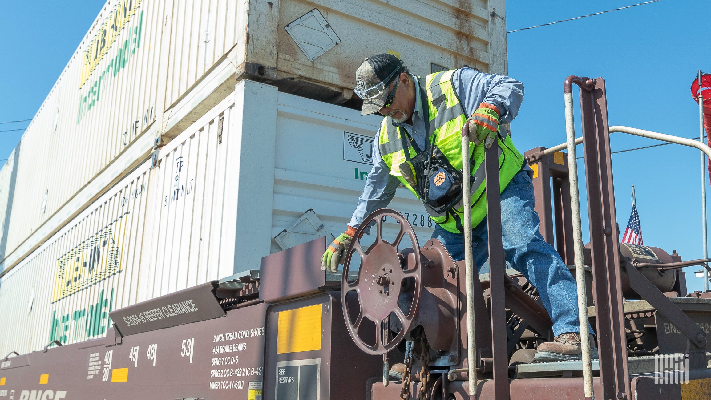 A photograph of a man turning the steel wheel of an intermodal car.