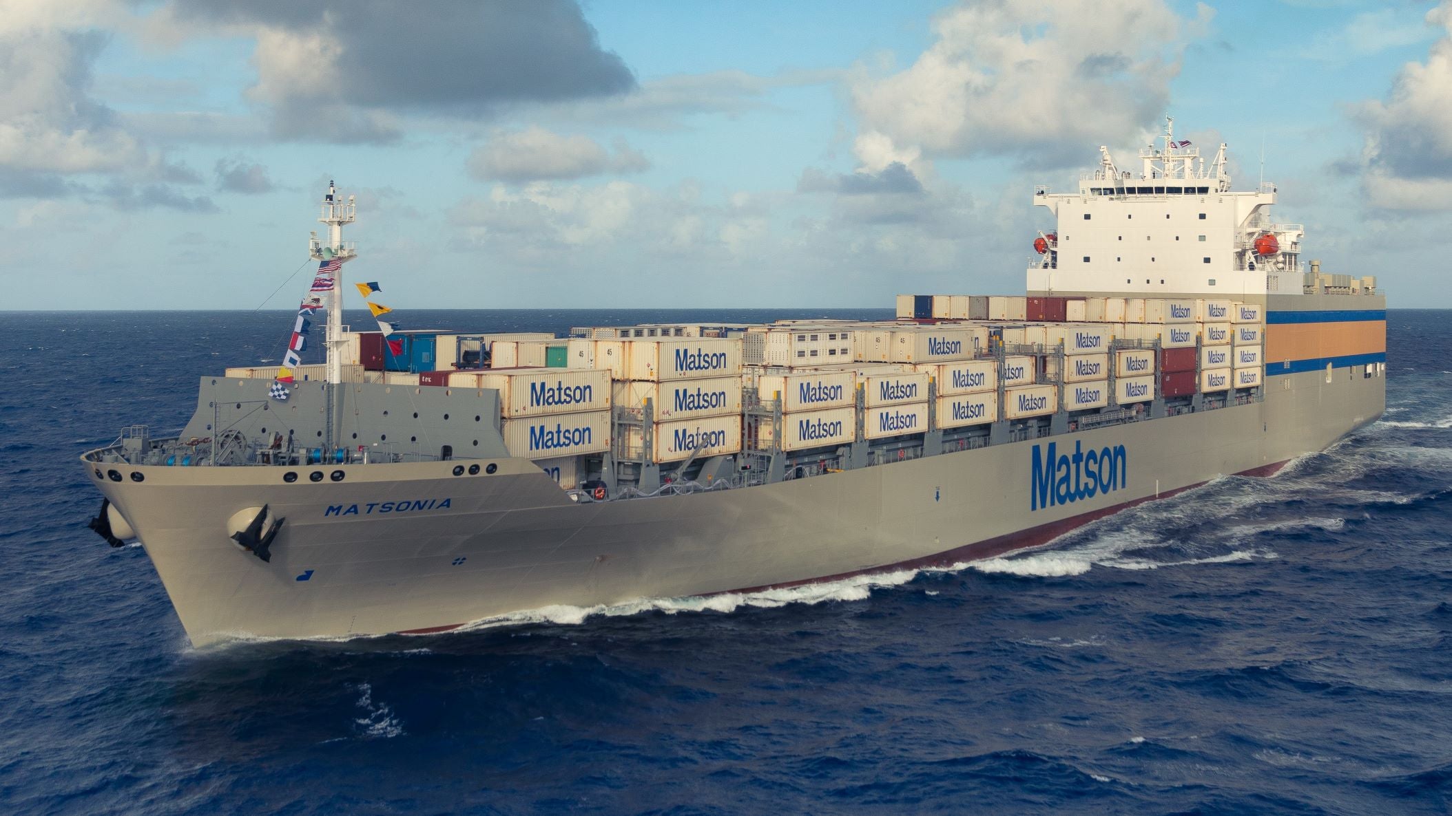 A container vessel riding the open ocean under partly cloudy skies.