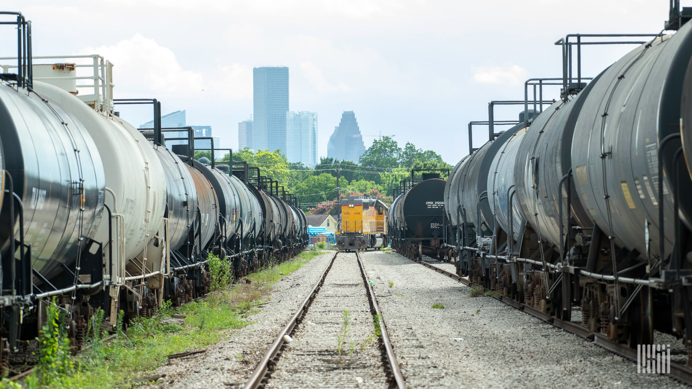 A photograph of a freight train locomotive flanked by two lines of railcars in a railyard.