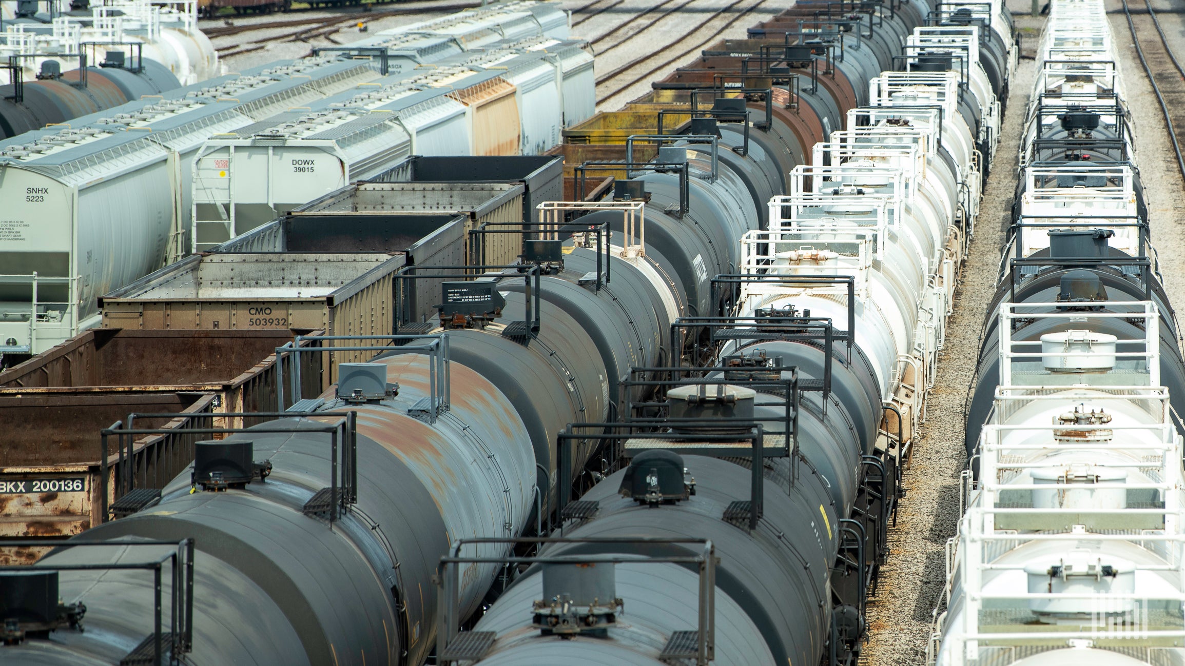 A photograph of a tank cars and grain hoppers parked in a rail yard.