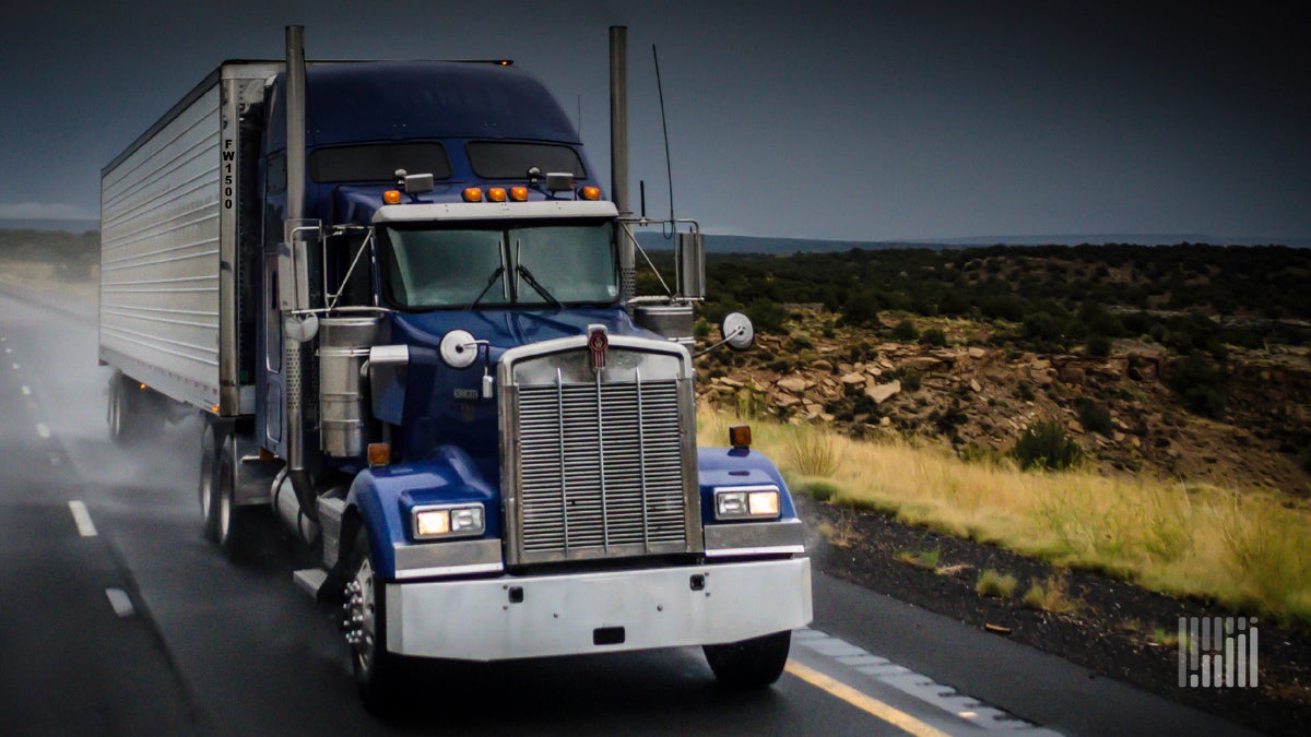 Tractor-trailer heading down a wet highway.