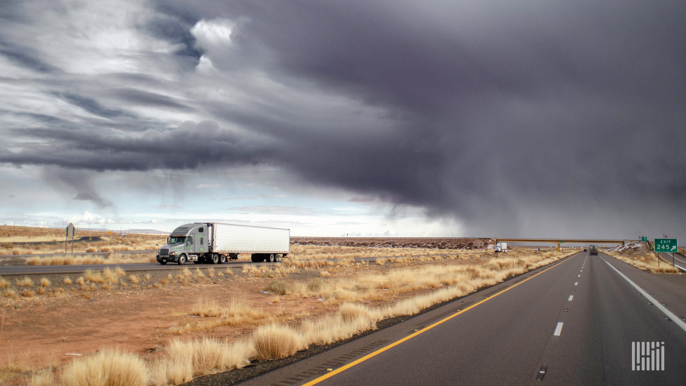 Thunderstorm behind a tractor-trailer on a highway.