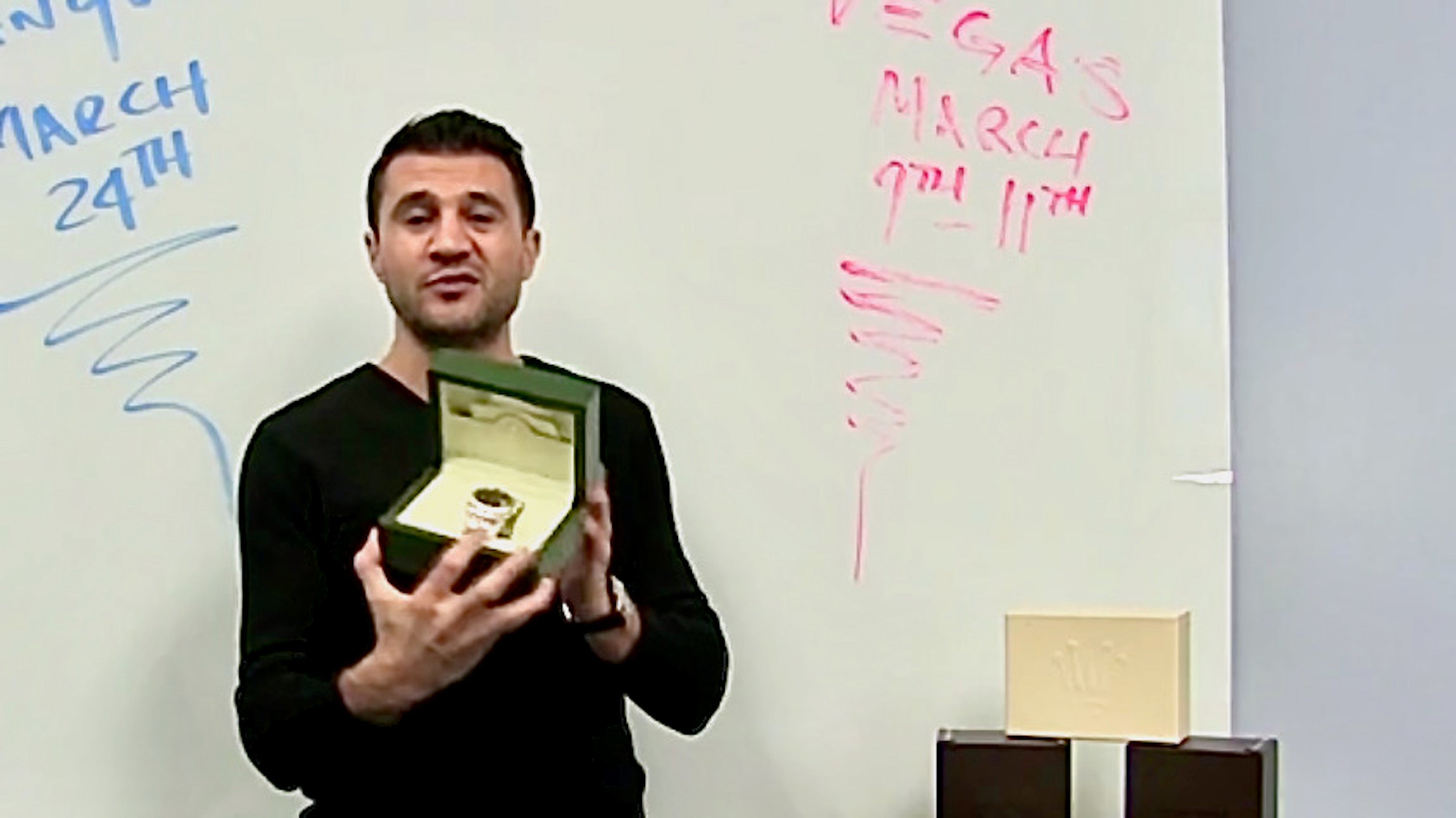 A man, All State Association CEO Steve Avetyan, holding a Rolex watch in front of a white board.