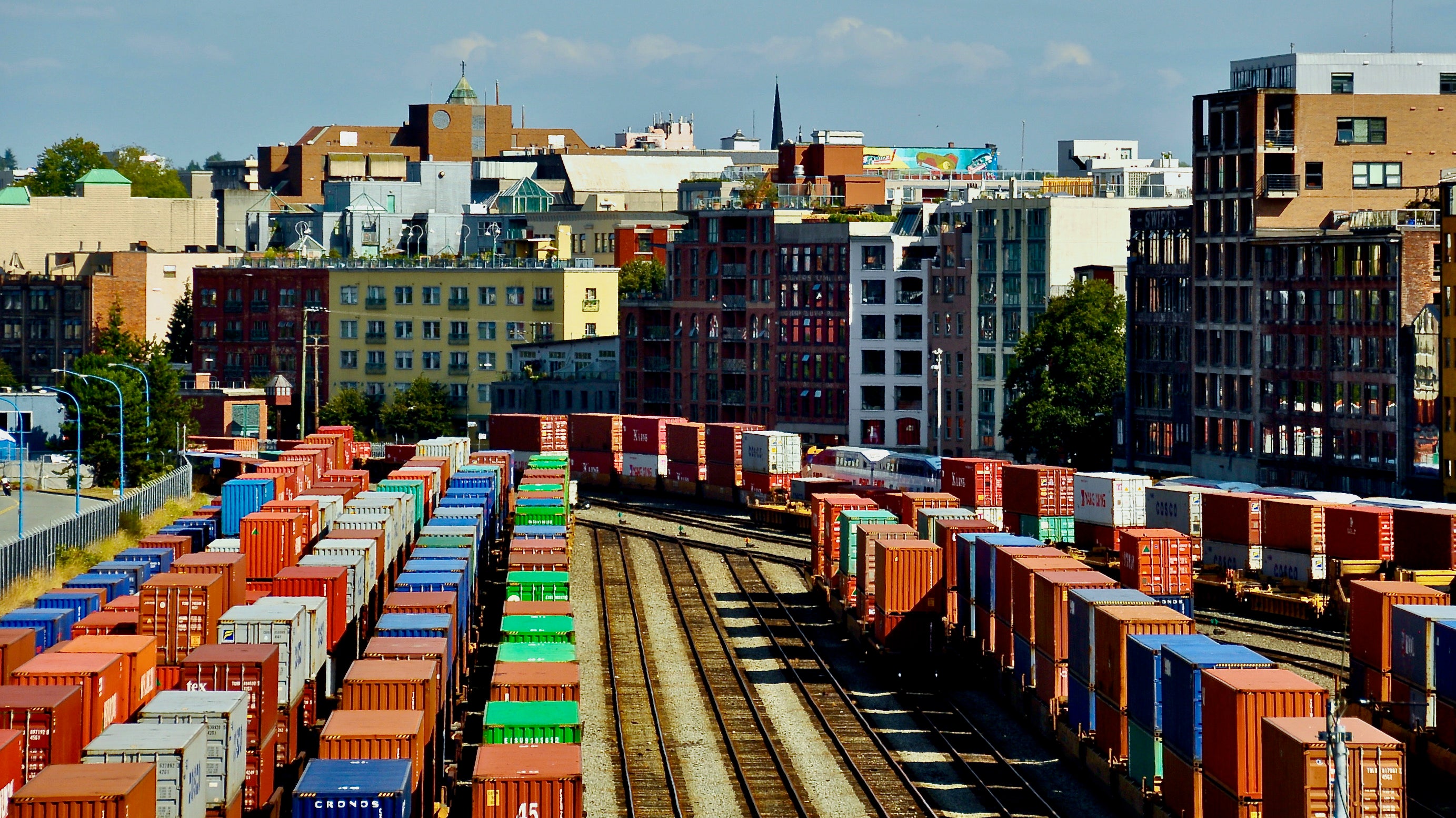 Rail cars loaded with intermodal containers near the port of Vancouver, with the city skyline behind it.