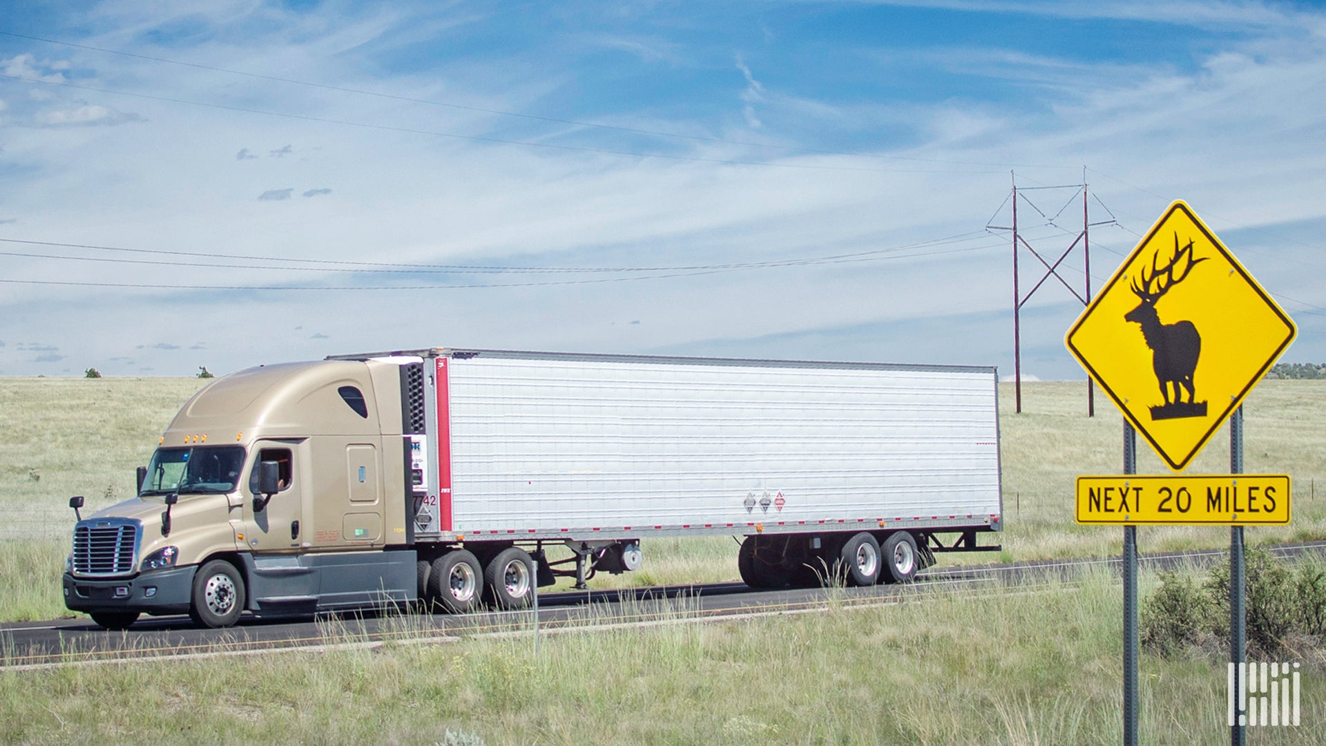 Tractor-trailer on a highway with a deer crossing sign in the foreground.