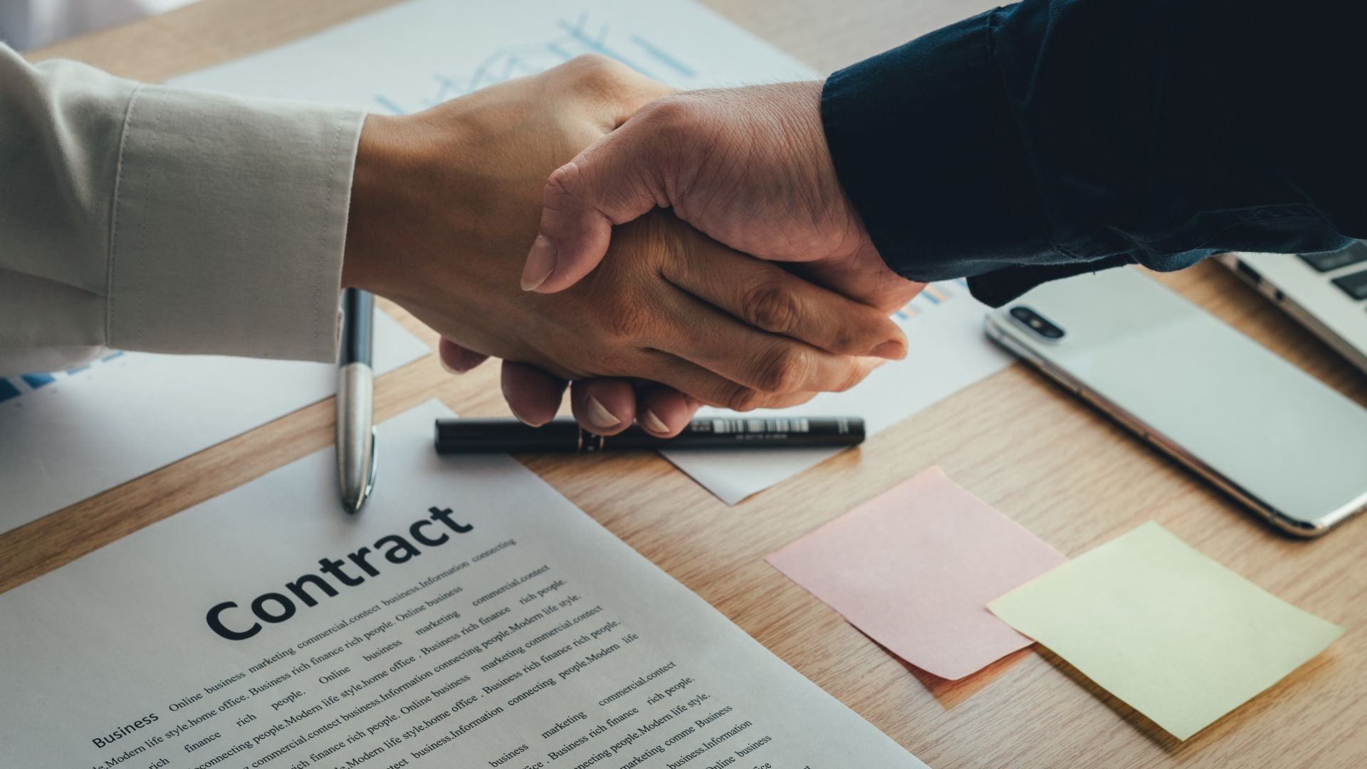 A handshake over a contract lying on table.