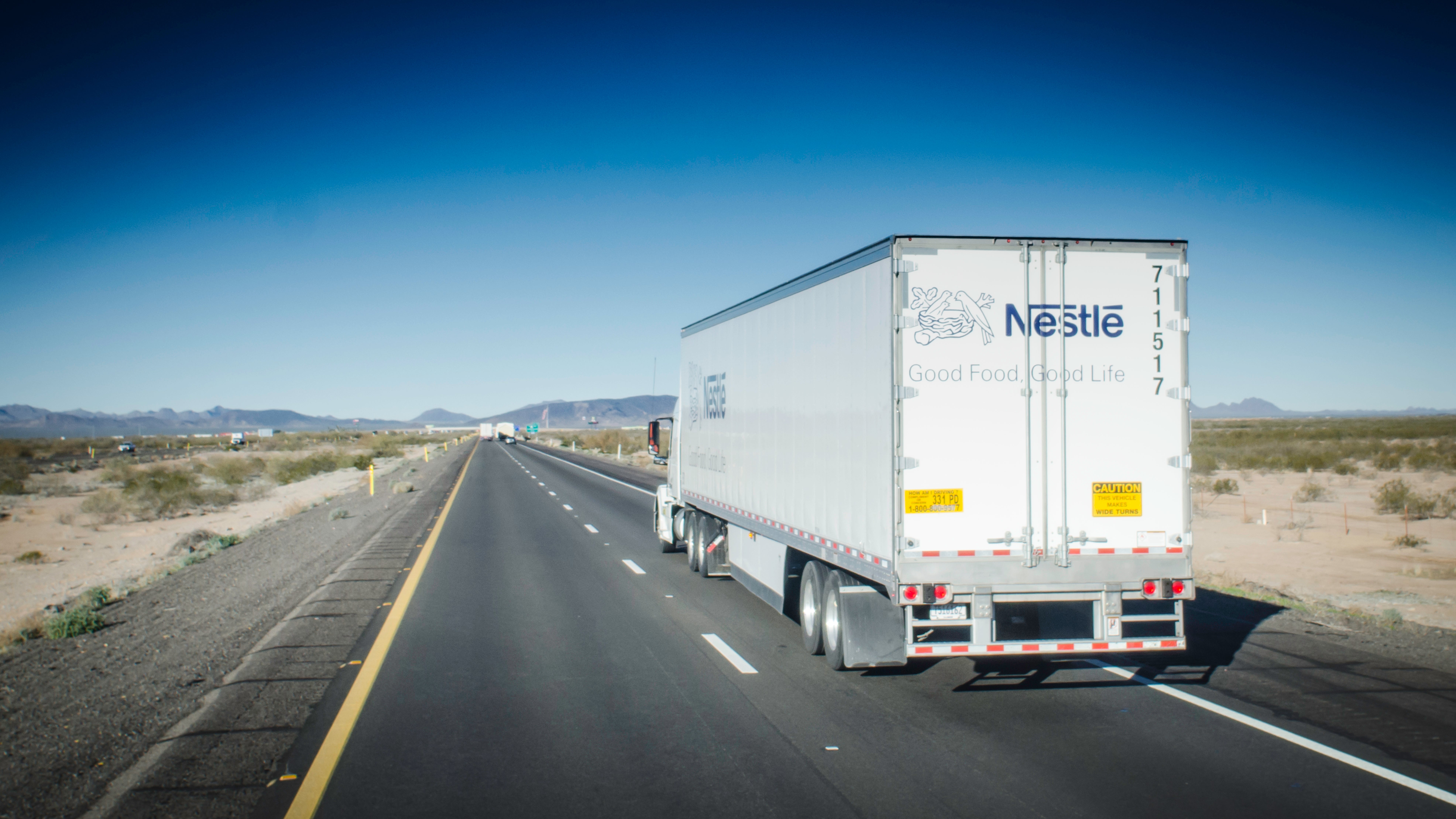 A photograph of a truck traveling down a highway in the desert.