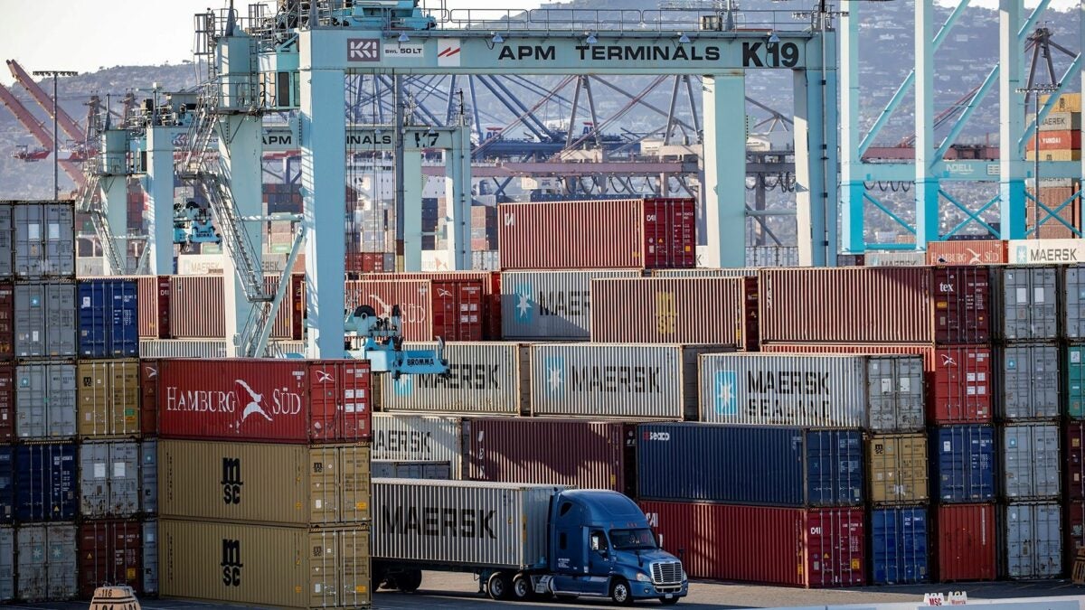 A truck driving through large stacks of containers at a port.