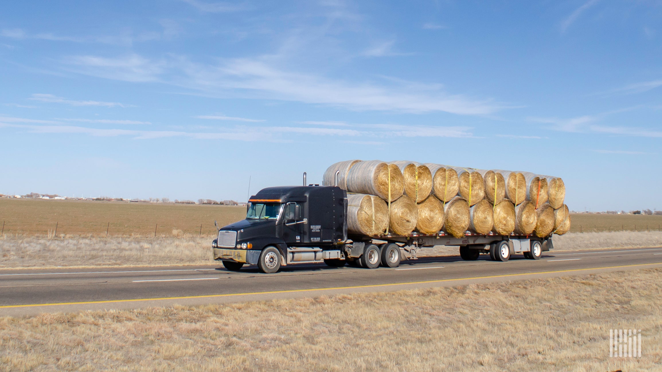 Flatbed truck carrying large bales of hay.