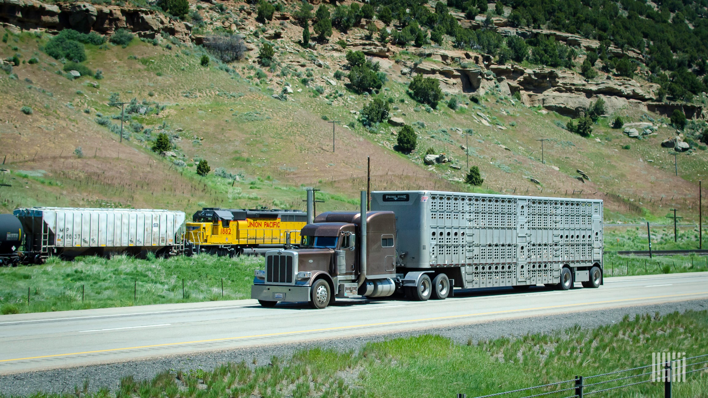 A photograph of a truck on a highway and a train in the background.