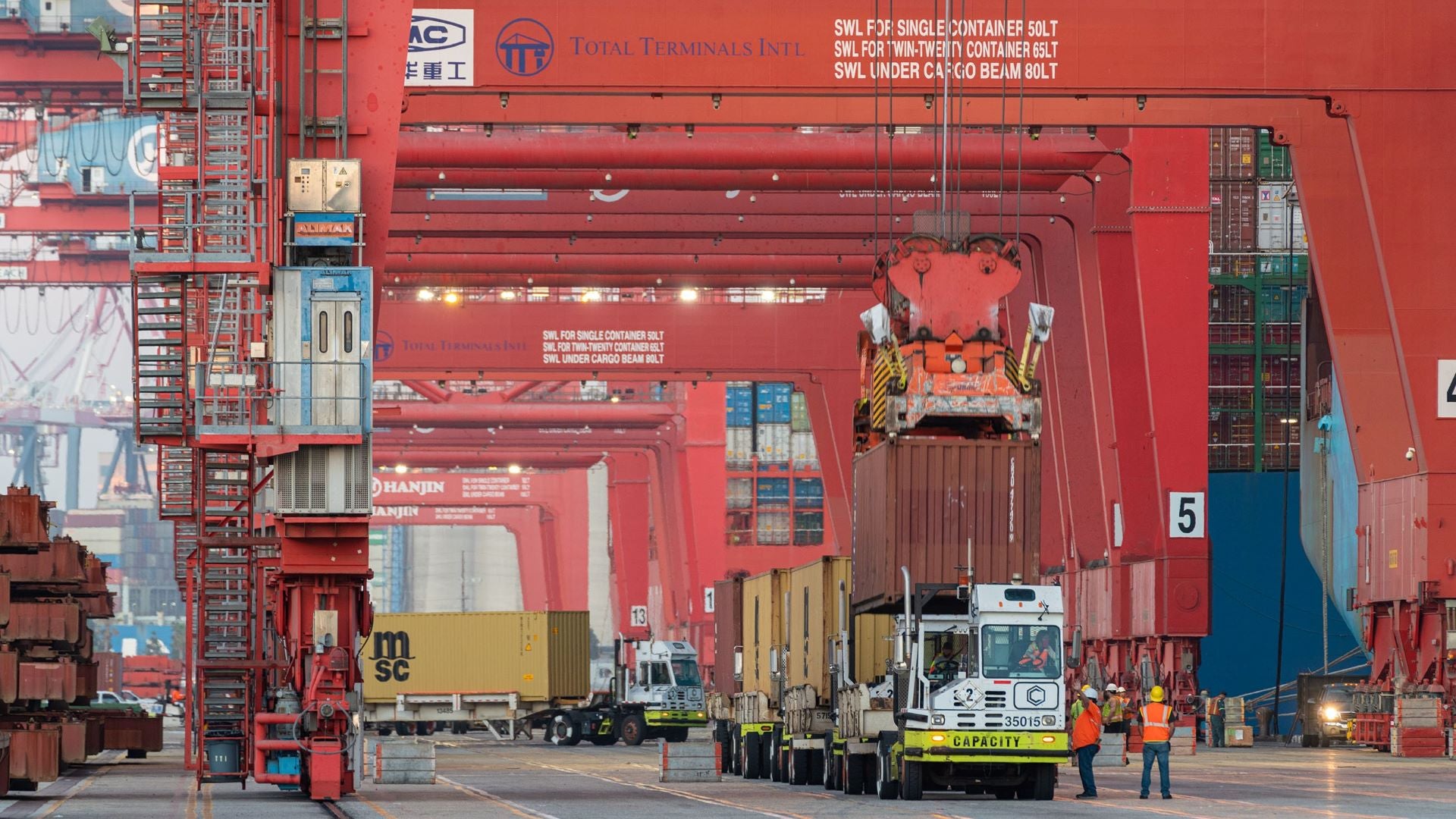 Giant cranes maneuver containers onto yard dollies on the dock.