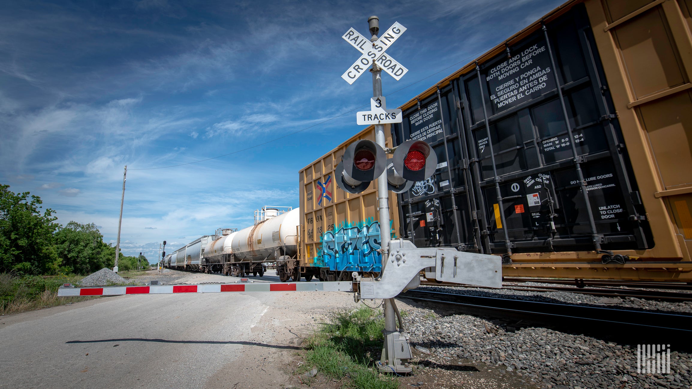 A photograph of a train at a rail crossing.