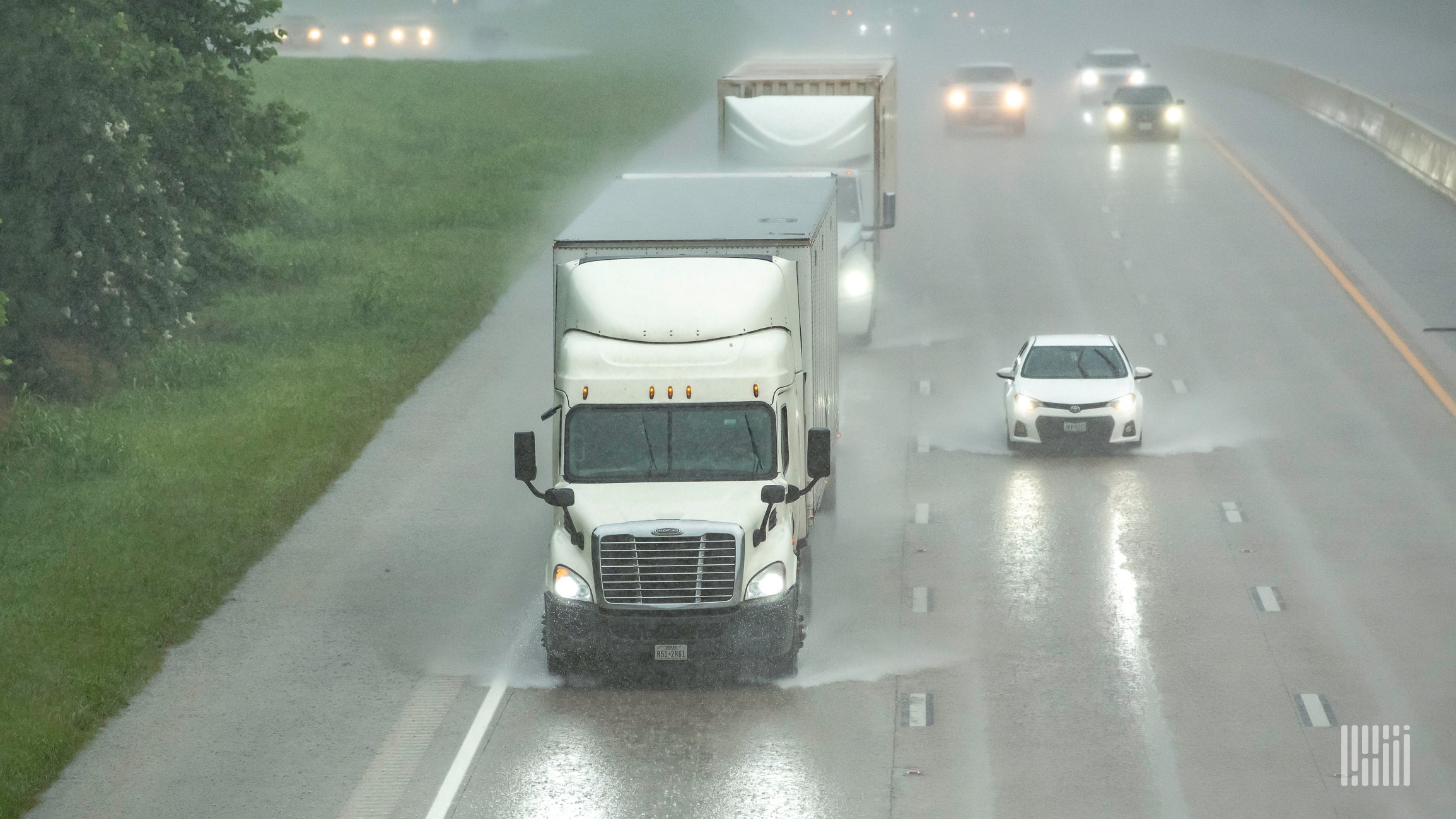 Tractor-trailers on a highway in heavy rain.