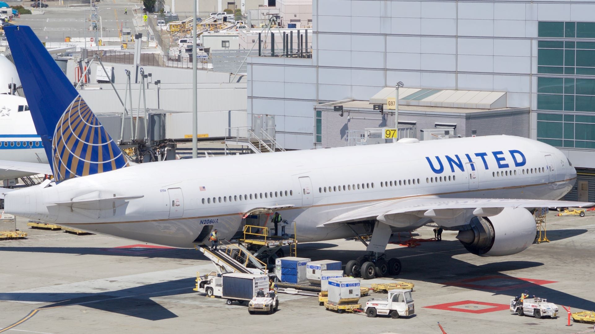 A United Airlines jet at the airport gate with cargo containers on the tarmac ready for loading.