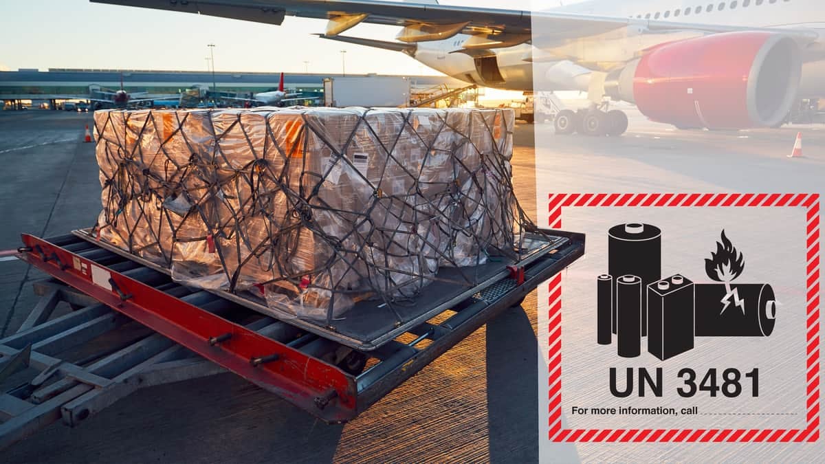 A pallet of cargo sits on tarmac near airplane with a hazardous goods warning label on it.