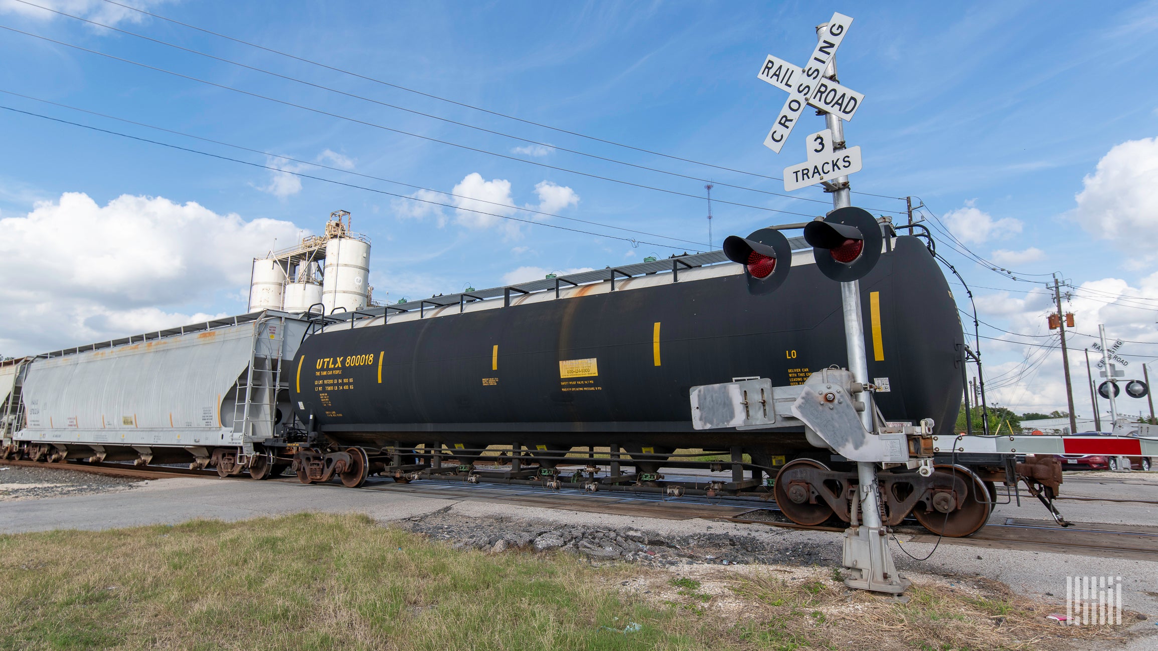 A photograph of a train passing by a rail crossing.