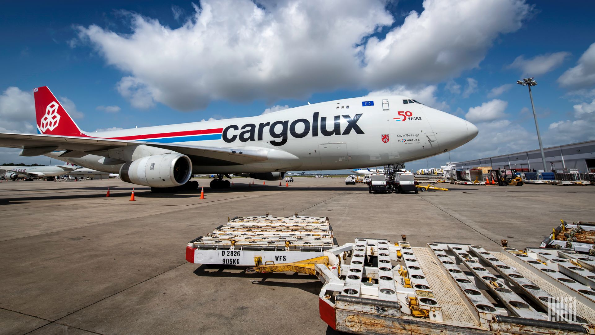 A Cargolux 747 cargo plane on the tarmac on a bright day with an empty pallet in the foreground.