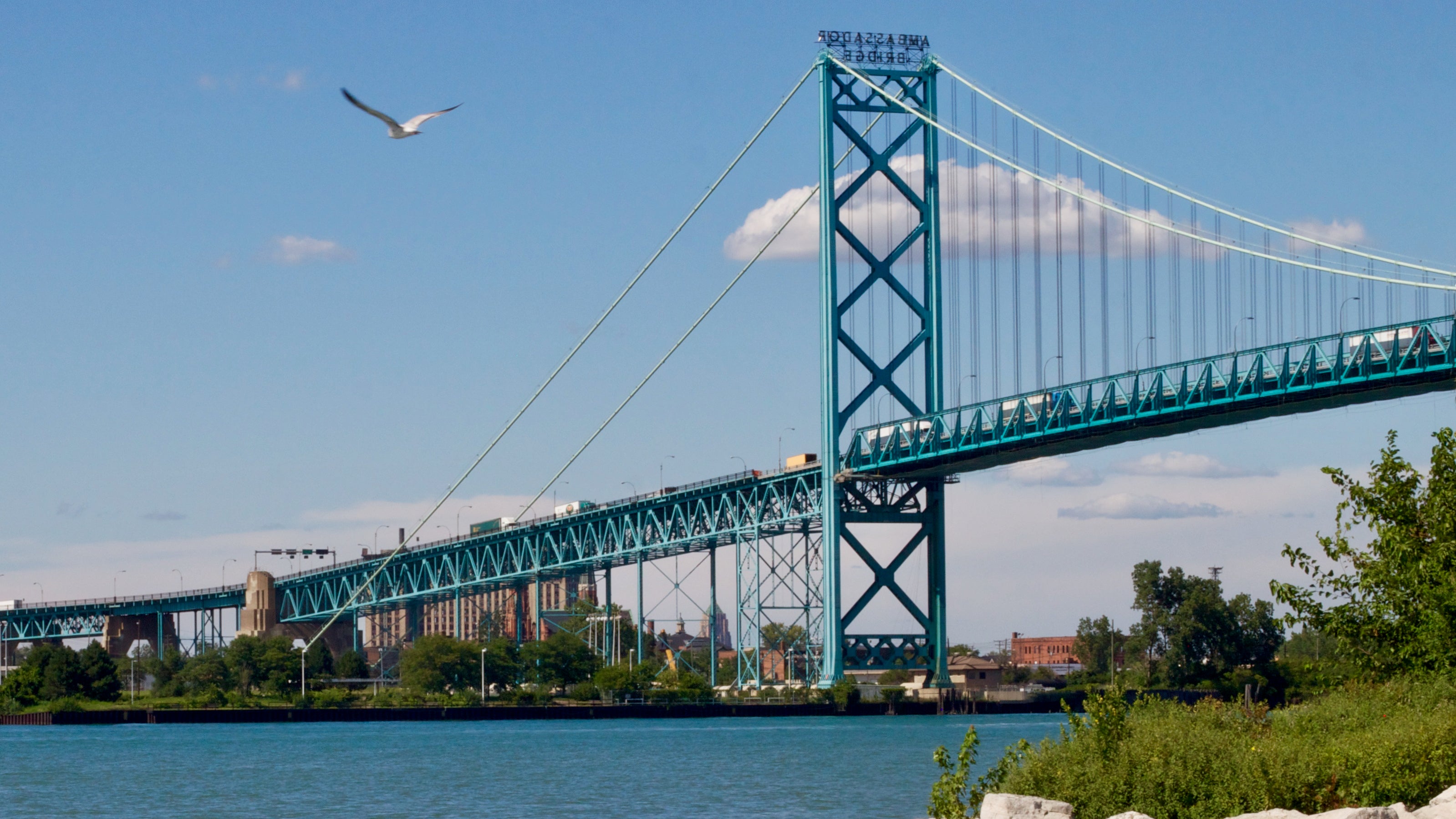 Trucks cross the Ambassador Bridge, a suspension bridge, seen from below.