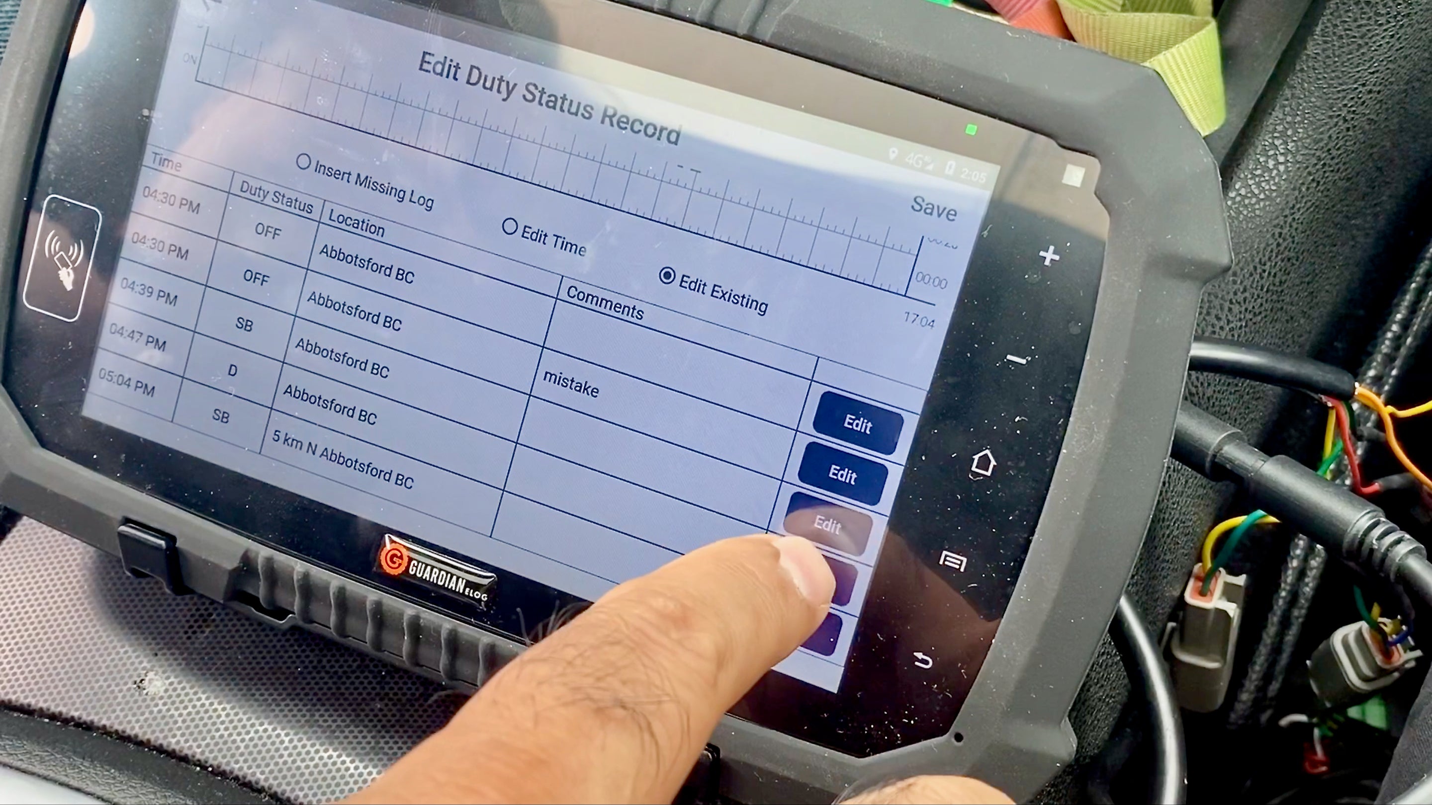 An electronic logging device screen being edited, with a finger being shown pushing a button on the screen.