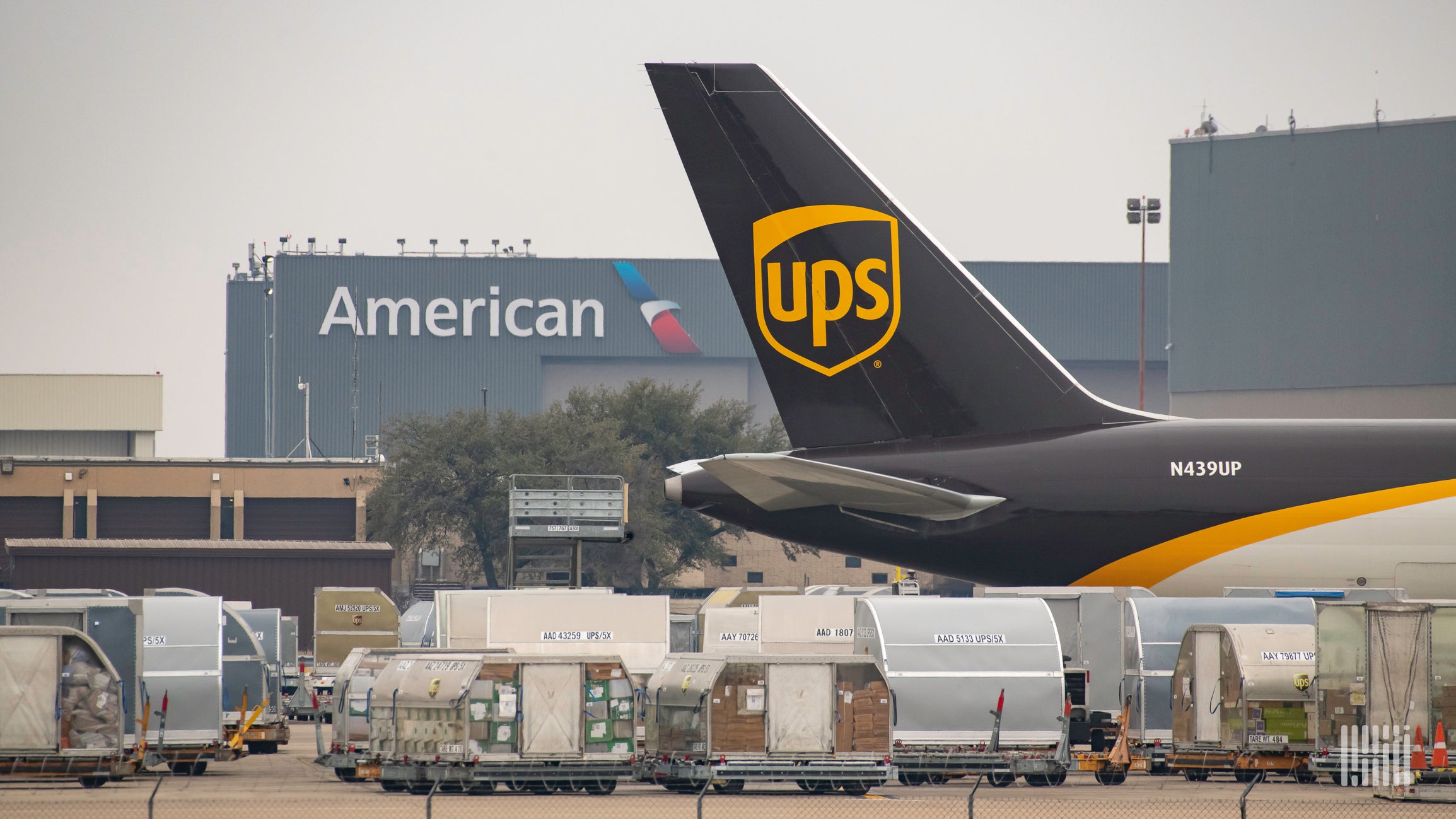 A UPS plane's tail at an airport with air cargo below to illustrate an article about cybersecurity reporting requirements for the rail and air sectors.