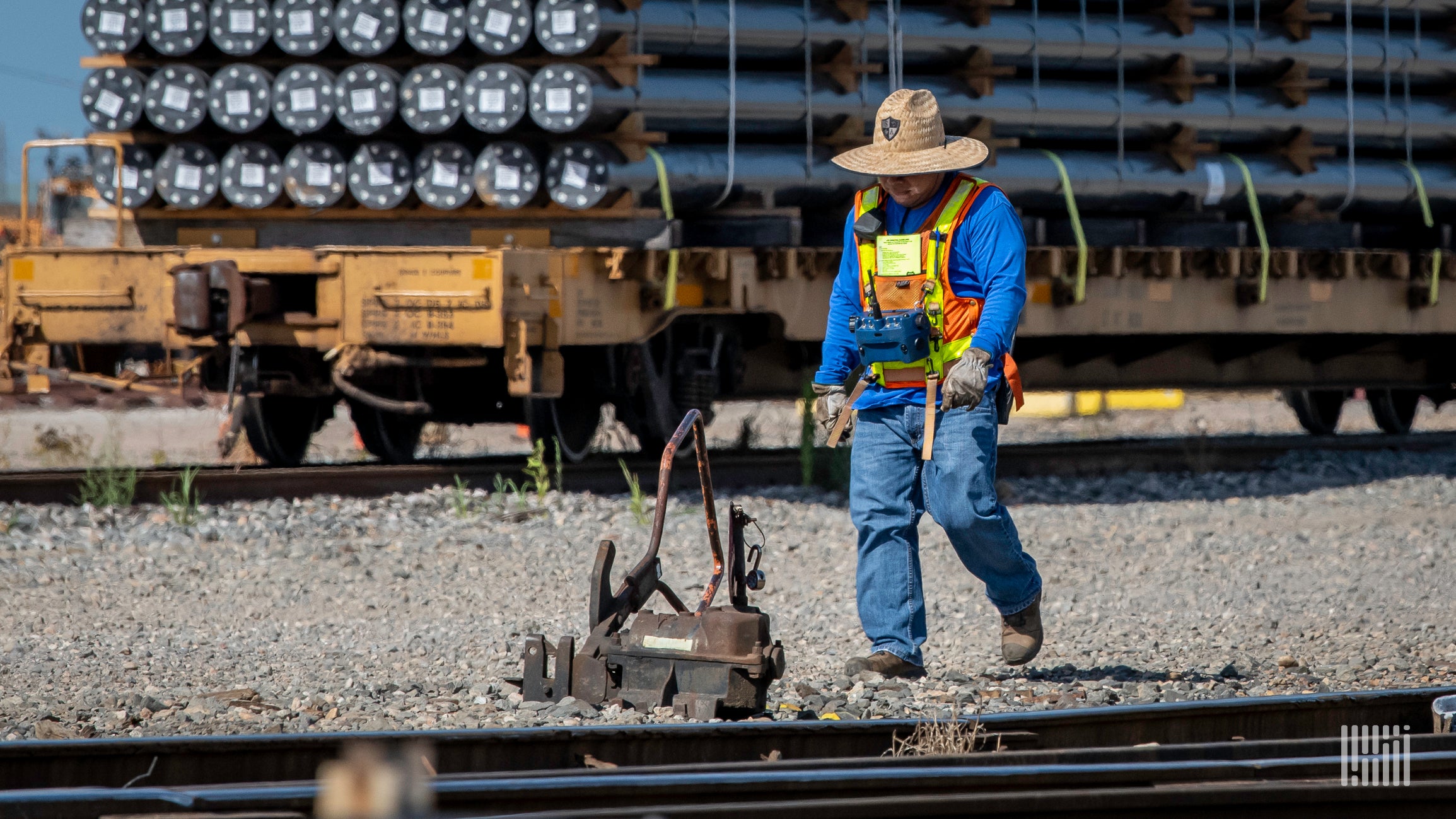 A photograph of a man looking at piece of railroad equipment in a rail yard.