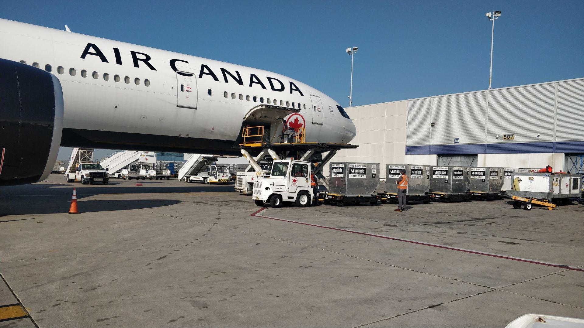 White Air Canada jet with cargo containers on the ground ready to load. Photo from side looking to forward half of the plane.