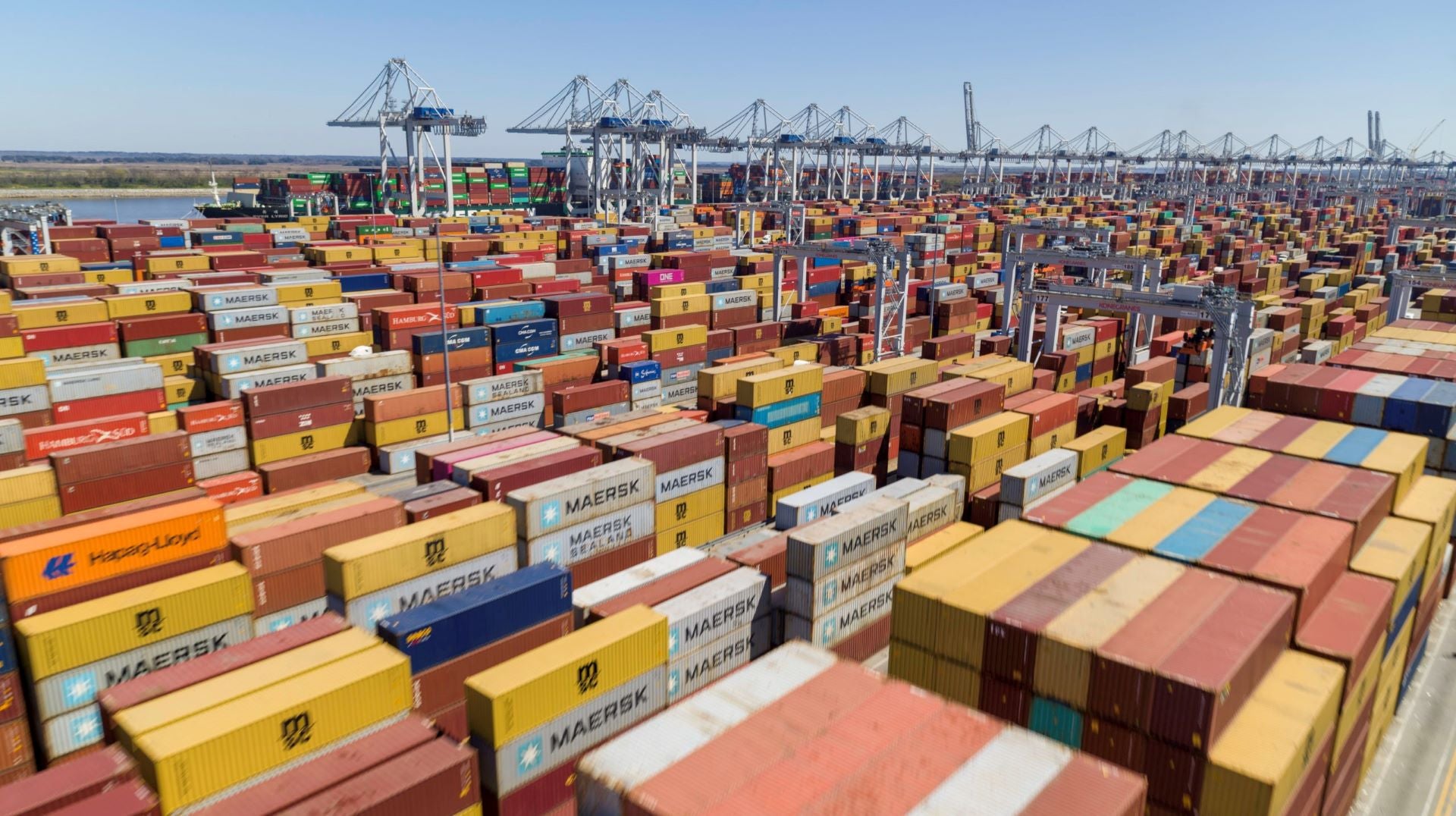 Huge stacks of orange and other colored-containers at a port, with cranes in the background.