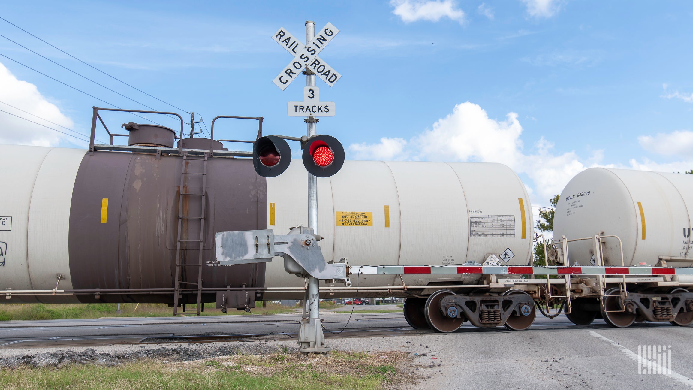 A photograph of a freight train rolling by a rail crossing.