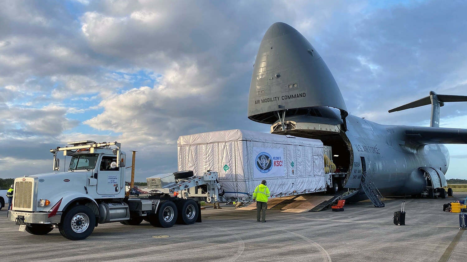 An 18-wheeler unloads the GOES-T satellite from a military plane.