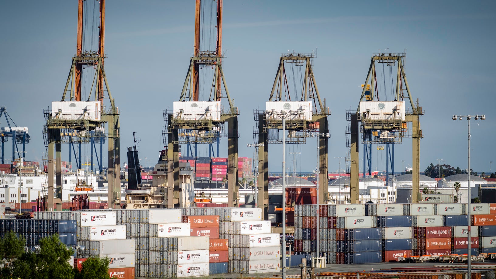 Stacks of containers at a port and cranes in the background.